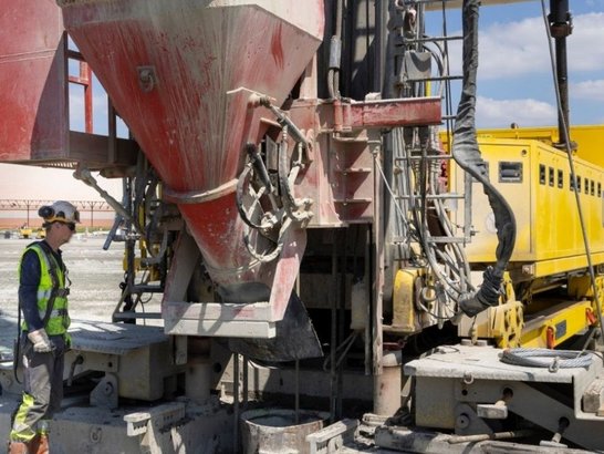 Bild zeigt eine Baustelle. Ein Bauarbeiter steht vor einem groĂen BaugerĂ€t