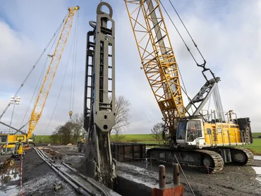 Bild zeigt einen Schlitzwandgreifer der gerade im Einsatz ist. Im Hintergrund sieht man grüne Wiesen.