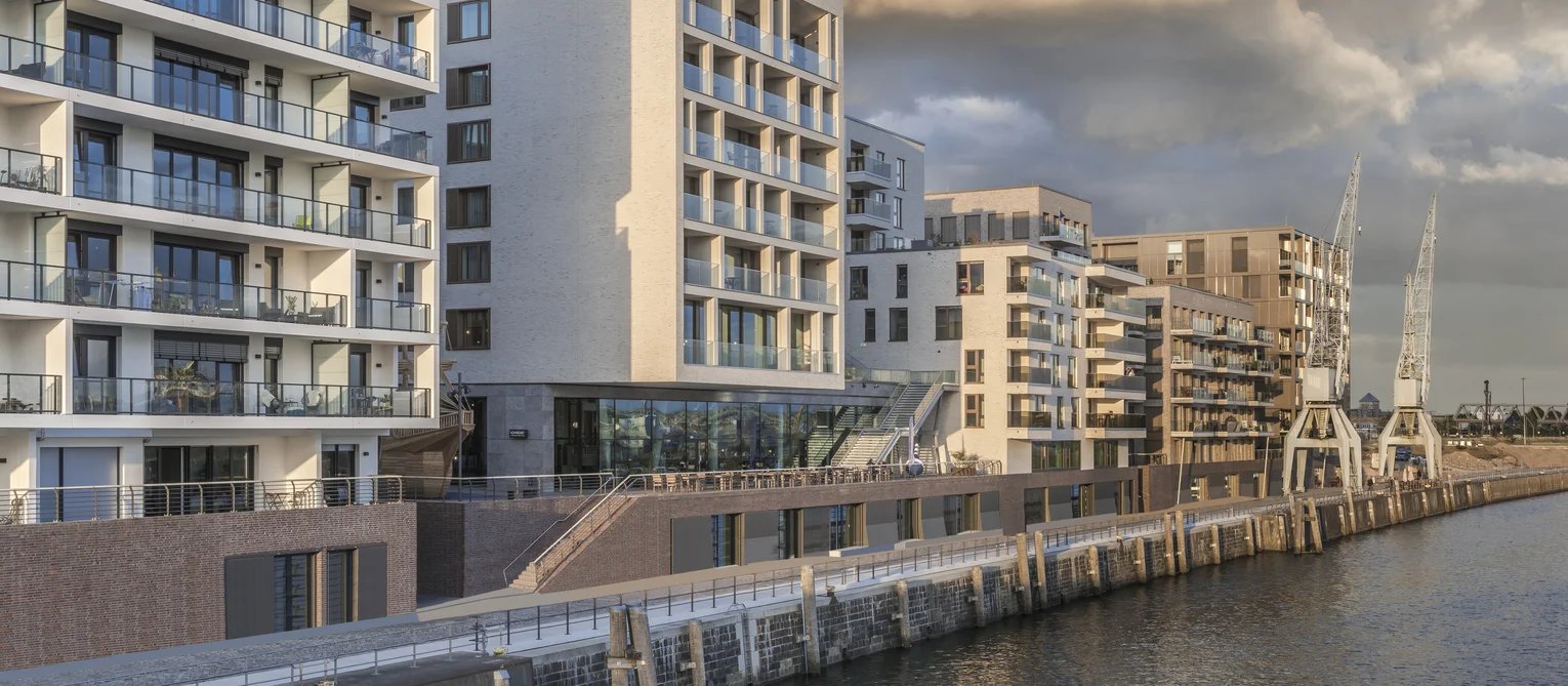 The building is located directly on the waterfront of Hamburg harbour. The building has a smooth sand-coloured façade with glazed balconies.