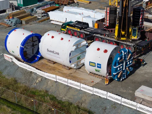 Auf dem Bild sieht man die Tunnelbohrmaschine und das Schneidrad aus der Vogelperspektive. Ein Mann steht daneben und überwacht die Montage.