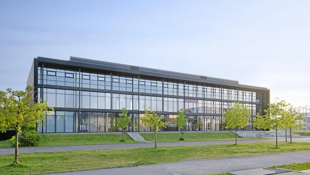 View of the rear of the building; 3 green areas separated by a staircase and pedestrian walkways; the light-flooded, 3-storey extension can be seen; glass front