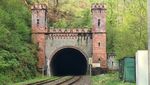 Blick auf einen historischen Tunneleingang, durch den eine Bahnstrecke führt.