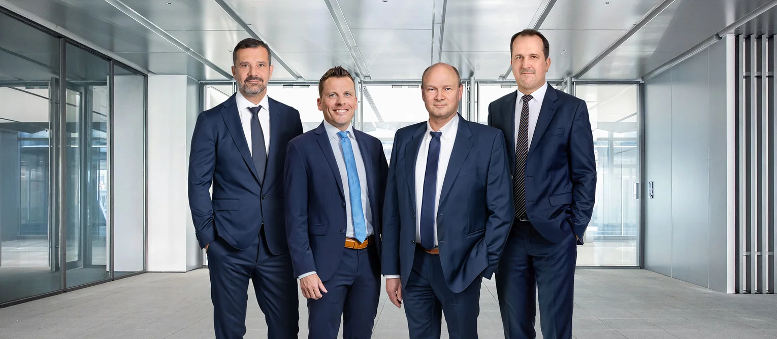 The image shows a group photo of the management team. It shows four men wearing suits and ties.