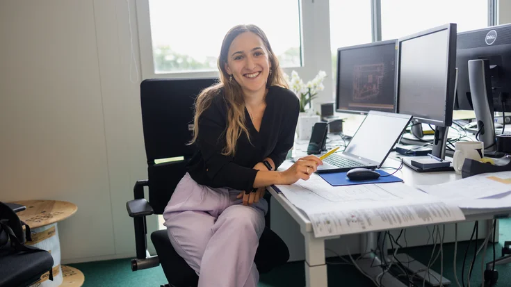 The picture shows a woman at a desk. She is smiling at the camera.