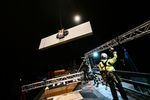 Picture shows a crane pulling up façade insulation. A man wearing a climbing harness and helmet is signalling to the crane operator. The picture was taken at night. 