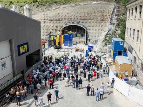 Auf dem Bild sieht man die Tunnelanschlagfeier, die vor dem Eingang des Tunnels am Pumpspeicherkraftwerk Forbach stattfindet. Viele Menschen hören einem Redner zu.