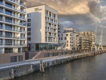 The building is located directly on the waterfront of Hamburg harbour. The building has a smooth sand-coloured façade with glazed balconies